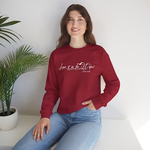Op de afbeelding: Een rood sweatshirt met witte tekst die "Leave it in the Water!" en "Acts 2:38" zegt.