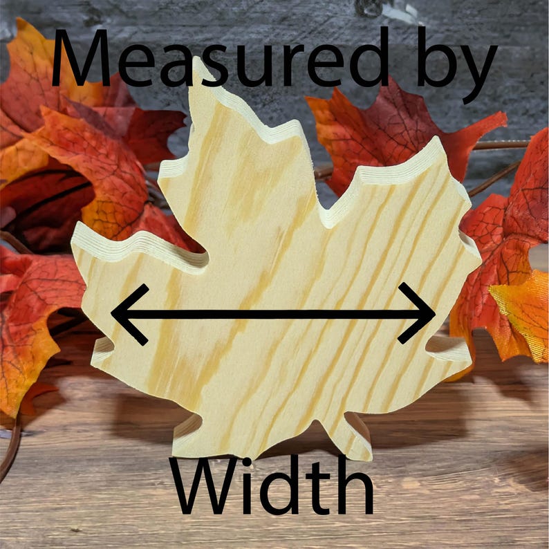 May include: A wooden maple leaf cutout with the word "Width" and the text "Measured by" in black. The leaf is light brown with visible wood grain. Arrows indicate the width measurement. Autumn leaves are in the background.