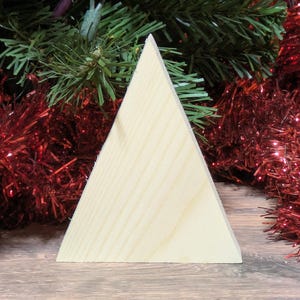 May include: A triangular wooden block with a light tan natural wood grain finish. The object features a flat base and two angled sides meeting at a point at the top, displaying a smooth surface texture and visible wood grain patterns throughout.