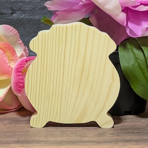 May include: A wooden, light-colored, decorative pot-shaped item with a scalloped top and curved base. The pot has a natural wood grain pattern and is set against a backdrop of pink and purple flowers.