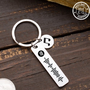 May include: Silver keychain with a music note charm and a rectangular tag with a Spotify logo and a barcode. The tag is engraved with a barcode.