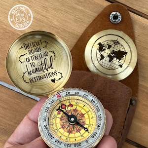 May include: A brass compass with a quote engraved on the lid: "Difficult roads often lead to beautiful destinations". The compass has a world map design on the bottom and a traditional compass face with a black needle.
