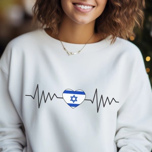 May include: White sweatshirt with a black and blue heart-shaped graphic of the Israeli flag with a heartbeat line on either side. The text "Israel" is not visible in the image.