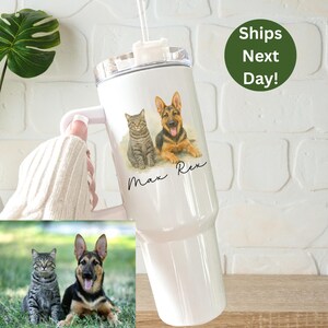 May include: White stainless steel tumbler with a lid and handle. The tumbler has a personalized design featuring a cat and a dog with their names "Max" and "Rex" written below.