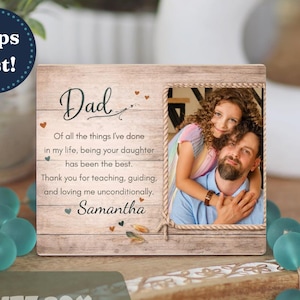 May include: Wooden photo frame with a picture of a father and daughter. The frame has the word "Dad" and a personalized message. The frame is decorated with small hearts and the name "Samantha".
