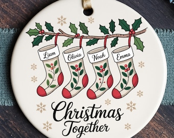 May include: A round Christmas ornament with a festive design. It features four hanging stockings, each with a name: Liam, Olivia, Noah, and Emma. The ornament has a holly branch and the words "Christmas Together".