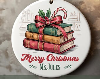 May include: A white ceramic Christmas ornament with a stack of books, a candy cane, and a red bow. The ornament says "Merry Christmas Ms. Jules" in red script. The books are green, orange, and red.