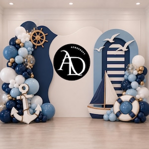 May include: Nautical-themed party backdrop with navy blue, light blue, and white balloons, a wooden ship's wheel, and an anchor. A sailboat, life preserver, and seagulls complete the scene. The backdrop features the text "ATDSCRAFT" in a black circle.