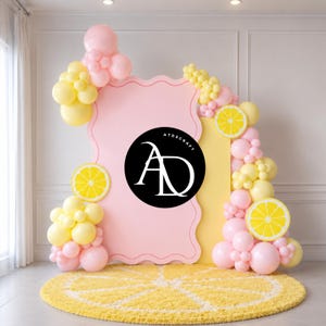 May include: A decorative backdrop featuring a pink wavy-edged frame, yellow and pink balloons, and lemon slice accents. A yellow rug shaped like a lemon slice is on the floor. The backdrop has the text "ATDSCRAFT" in a black circle.