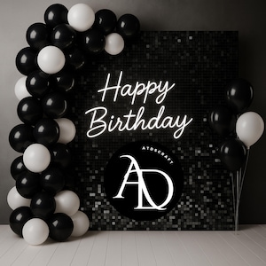 May include: A black and white balloon arch frames a black sequined backdrop with the words "Happy Birthday" in white neon. A black circle with the letters "AD" is at the bottom. Additional black and white balloons are on the right.