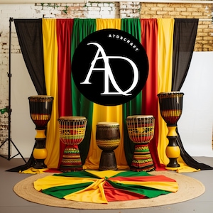May include: Four traditional African drums with black, red, yellow, and green patterned designs, set up on a stage with a backdrop of black, yellow, red, and green fabric. The stage is decorated with a circular rug with the same colors. The logo "ATDSCRAFT AD" is displayed on the backdrop.
