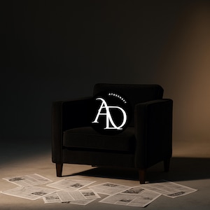 Puede incluir: Un sillón negro de diseño cuadrado, sobre un fondo oscuro. Un logotipo circular con el texto "ATOSCRAFT" y las letras "AD" está colocado en la silla. Periódicos esparcidos en el suelo.