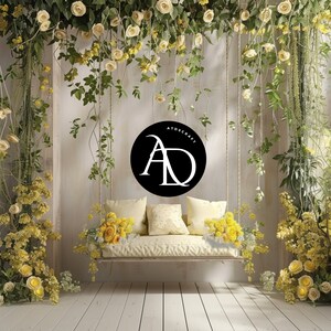 May include: A white swing with yellow floral accents hangs in front of a white wall decorated with a black circle with the text "ATDSCRAFT" and the letters "AD" in white. The swing is surrounded by yellow flowers.