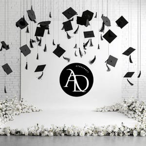 May include: A white brick wall backdrop with a white surface in front of it. Black graduation caps hang from the ceiling. White flowers are on the floor in front of the surface. A black circle with the text "ATDSCRAFT AD" is in the center of the surface.