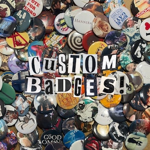May include: A collection of round pin-back badges featuring various graphic designs, movie posters, and text, including the words "CUSTOM BADGES!" overlaid in a bold, black and white ransom-note style font across the centre of the pile.