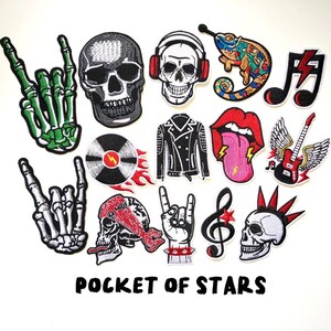Peut inclure: Un ensemble de 13 patchs thermocollants représentant divers motifs sur le thème du rock and roll, notamment des crânes, des notes de musique, une guitare, un caméléon et une main faisant le signe du rock and roll. Les patchs sont colorés et présentent une variété de textures. Le texte "POCKET OF STARS" est imprimé sous les patchs.