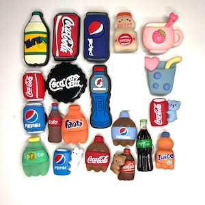 Op de afbeelding: Een verzameling kleurrijke, miniatuur, plastic bedels met populaire drankmerken zoals Coca-Cola, Pepsi, Sprite en Fanta. De bedels bevatten ook een melkpak, een yoghurtbeker en een sappak.