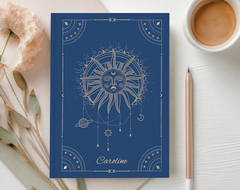 May include: A blue notebook with a gold sun and celestial design. The notebook has the name "Caroline" written on the front.