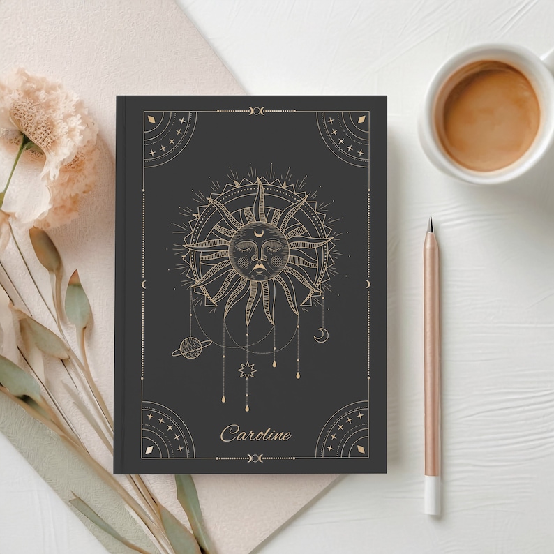 May include: Black notebook with a gold sun and moon design. The notebook has the name "Caroline" written on the front.