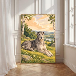 May include: A framed wall art print featuring a grey Irish Wolfhound lying in a grassy meadow. The scene includes birch trees, rolling hills, a distant river, and a soft sunset sky with peach and yellow clouds above the dog.
