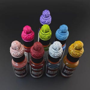 Op de afbeelding: Een verzameling van tien kleine flesjes verf met decoratieve doppen. De doppen zijn allemaal in verschillende kleuren en hebben een uniek ontwerp. De flesjes zijn gelabeld met "Vallejo Xpress Color".