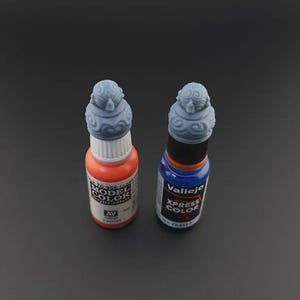 Op de afbeelding: Twee flessen verf met decoratieve doppen. De fles links is oranje en heeft "Model Color" op het etiket staan. De fles rechts is blauw en heeft "Vallejo Xpress Color" op het etiket staan.
