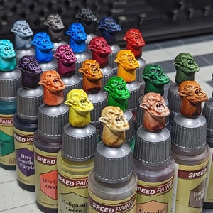 Op de afbeelding: Een verzameling van 20 kleine flesjes acrylverf met flesjes met een goblin-vorm. De flesjes zijn in twee rijen gerangschikt en zijn gelabeld met de verfkleur en "Speed Paint".
