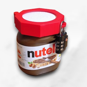 Pode incluir: Um frasco de Nutella com tampa vermelha e cadeado de combinação preto. O rótulo mostra uma fatia de pão com Nutella e avelãs. O frasco está em um fundo branco.