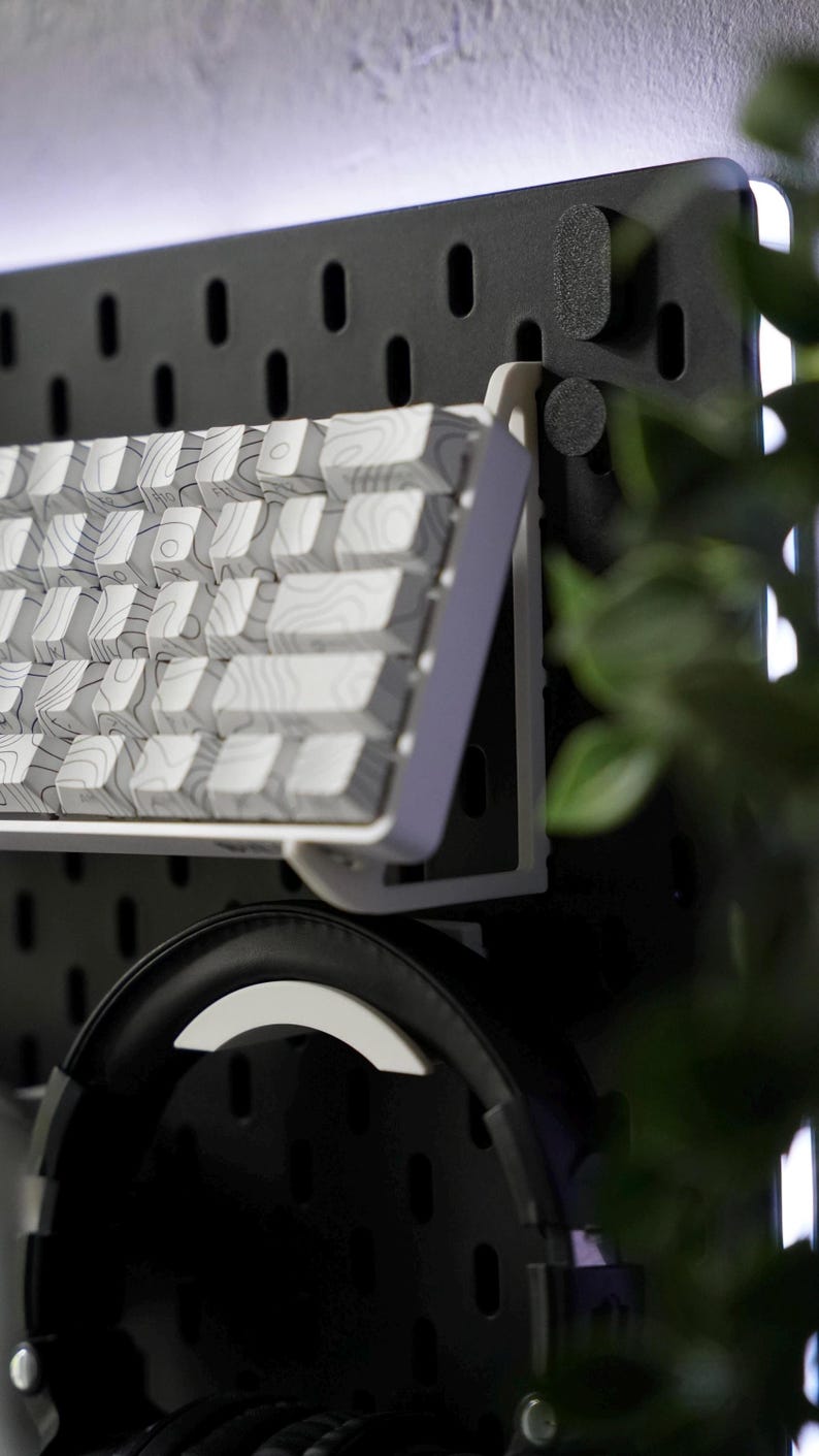 Puede incluir: Un teclado blanco con un patr&oacute;n de veta de madera est&aacute; montado en una pared de tablero de clavijas negro. Un par de auriculares negros cuelgan debajo del teclado.