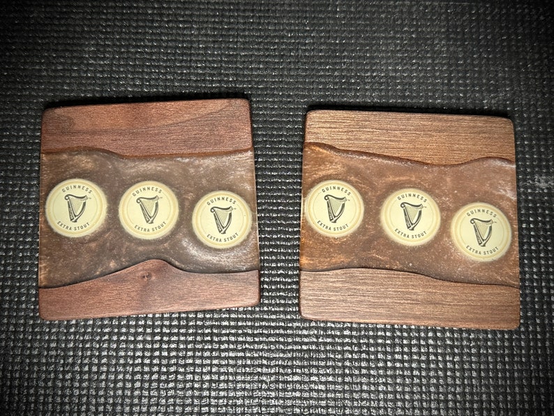 Pu&ograve; includere: Due sottobicchieri in legno con una macchia marrone e una parte superiore in resina epossidica trasparente. Ogni sottobicchiere ha tre tappi di bottiglia Guinness Extra Stout incorporati nella resina.