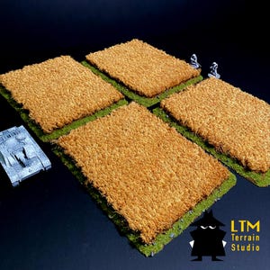 Puede incluir: Cuatro piezas de terreno rectangulares con una superficie marrón texturizada, bordeadas por hierba verde. Se ve un tanque en miniatura y dos figuras. El logotipo de LTM Terrain Studio está en la esquina inferior derecha.
