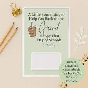 Puede incluir: Una tarjeta de regalo verde claro con el texto "A Little Something to Help Get Back to the Grind Happy First Day of School! Love, George." Hay una ilustración de una taza de café en la tarjeta. Un clip de papel dorado y lápices están a la izquierda.