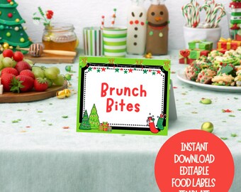 May include: A festive sign with the words "Brunch Bites" in red, framed in green and white, featuring Christmas motifs. The sign is on a table with food and drinks, including strawberries, grapes, and decorated bottles.