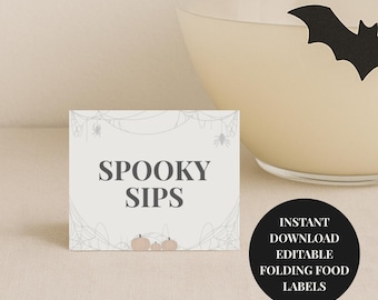 Op de afbeelding: Een rechthoekige kaart met de tekst "SPOOKY SIPS" in grijs, met een spinnenwebontwerp en kleine pompoenen. Een zwarte cirkel met witte tekst luidt "INSTANT DOWNLOAD EDITABLE FOLDING FOOD LABELS". Een glas met een vleermuissilhouet staat op de achtergrond.