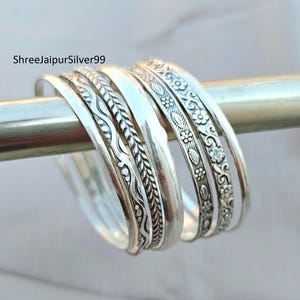May include: A collection of silver bangles with intricate floral and geometric patterns. The bangles are displayed on a silver rod, showcasing their detailed designs and polished finish. The text "ShreeJaipurSilver99" is visible.