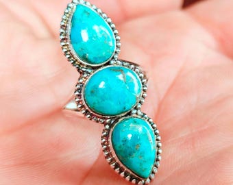 Peut inclure: Bague en argent ornée de trois pierres turquoises. Les pierres, en forme de goutte et ovale, sont serties dans une lunette perlée. La bague est une pièce de caractère avec une couleur bleu-vert vibrante.