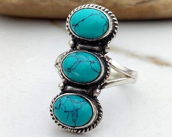 Peut inclure: Une bague en argent ornée de trois pierres ovales en turquoise. Chaque pierre est sertie dans une lunette texturée et détaillée. Le design de la bague est vertical, avec les pierres empilées. Les pierres de turquoise ont un aspect tacheté et vibrant.