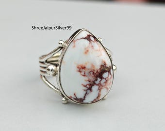 Peut inclure: Une bague en argent ornée d'une grosse pierre blanche en forme de goutte d'eau avec des veines marron. La bague a un design multi-bandes avec de petits accents ronds. Le texte "ShreeJaipurSilver99" est visible.
