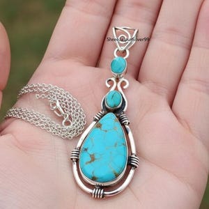 May include: A silver pendant necklace featuring a large, teardrop-shaped turquoise stone. The pendant has two smaller turquoise stones and decorative silver accents. The necklace chain is also silver.