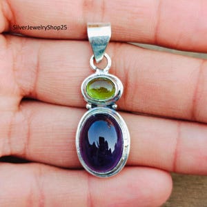 May include: A silver pendant with a purple and green gemstone. The pendant is oval shaped and has a silver bail.