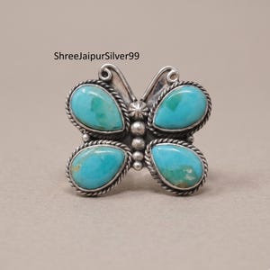 Peut inclure: Une bague en argent en forme de papillon, ornée de quatre pierres turquoise en forme de goutte, serties dans des bordures en fil torsadé. Le centre du papillon présente un détail en étoile et une rangée verticale de trois sphères en argent.