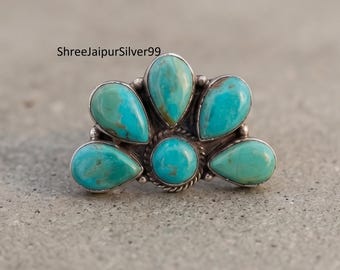 Peut inclure: Une bague en argent ornée de cinq pierres turquoise disposées en éventail. La pierre centrale est ronde, entourée de quatre pierres en forme de poire avec des motifs de matrice bruns visibles. Le sertissage inclut un détail en fil torsadé.