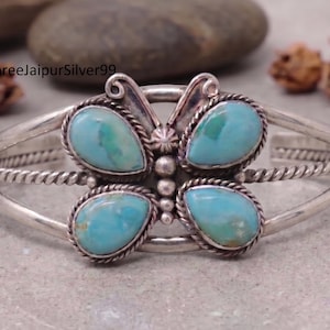 May include: A silver cuff bracelet featuring a butterfly design with four teardrop-shaped turquoise stones. The center of the butterfly is accented with small silver beads, and the band consists of twisted and smooth silver wire elements.