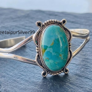 May include: A silver cuff bracelet featuring a large, oval turquoise stone. The turquoise is a vibrant blue-green with brown and yellow veining. The bracelet has a simple, elegant design, suitable for everyday wear.