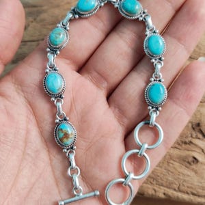 May include: A silver bracelet with oval turquoise stones. The stones are set in a decorative silver frame and linked with silver connectors. The bracelet has a toggle clasp. The text "ShreejaipurSilver99" is in the top left corner.