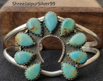 Peut inclure: Un bracelet manchette en argent orné de huit pierres turquoise en forme de goutte disposées en cercle autour d'une arche centrale en fil d'argent torsadé. Les pierres présentent des teintes bleu clair et vert avec des veines brunes.