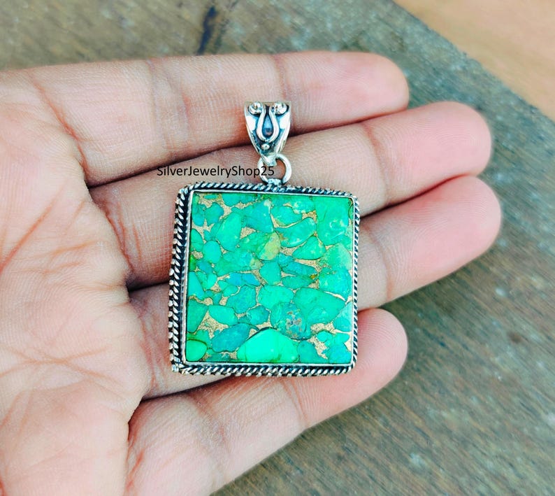 May include: A square turquoise pendant with a silver frame and a silver bail. The turquoise is a green and blue color with a marbled pattern.