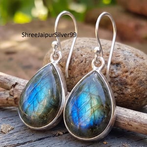 May include: Silver drop earrings with teardrop labradorite stones. The stones show iridescent blue and green colours, set in a polished silver bezel. The earrings have a simple, elegant design, suitable for everyday wear.