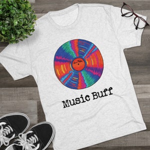 Puede incluir: Una camiseta blanca con un gráfico de disco de vinilo colorido y el texto "Music Buff" impreso en la parte delantera.