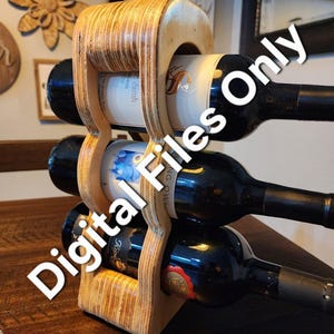 May include: A wooden wine rack with a natural finish holds three bottles of wine. The rack is shaped like a guitar and has a cutout for the neck of the bottle.